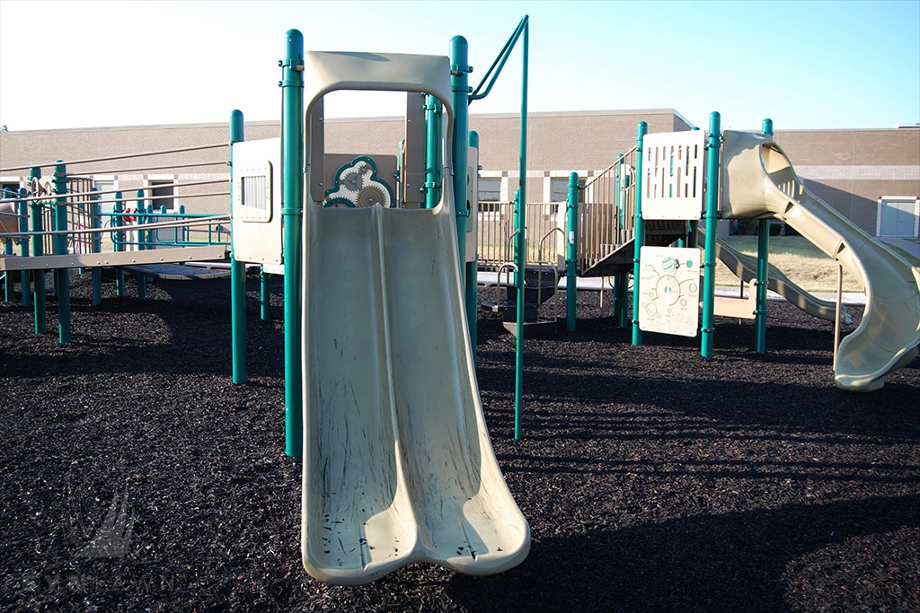image of prairie star elementary playground with a green curved double slide on top of rubber mulch