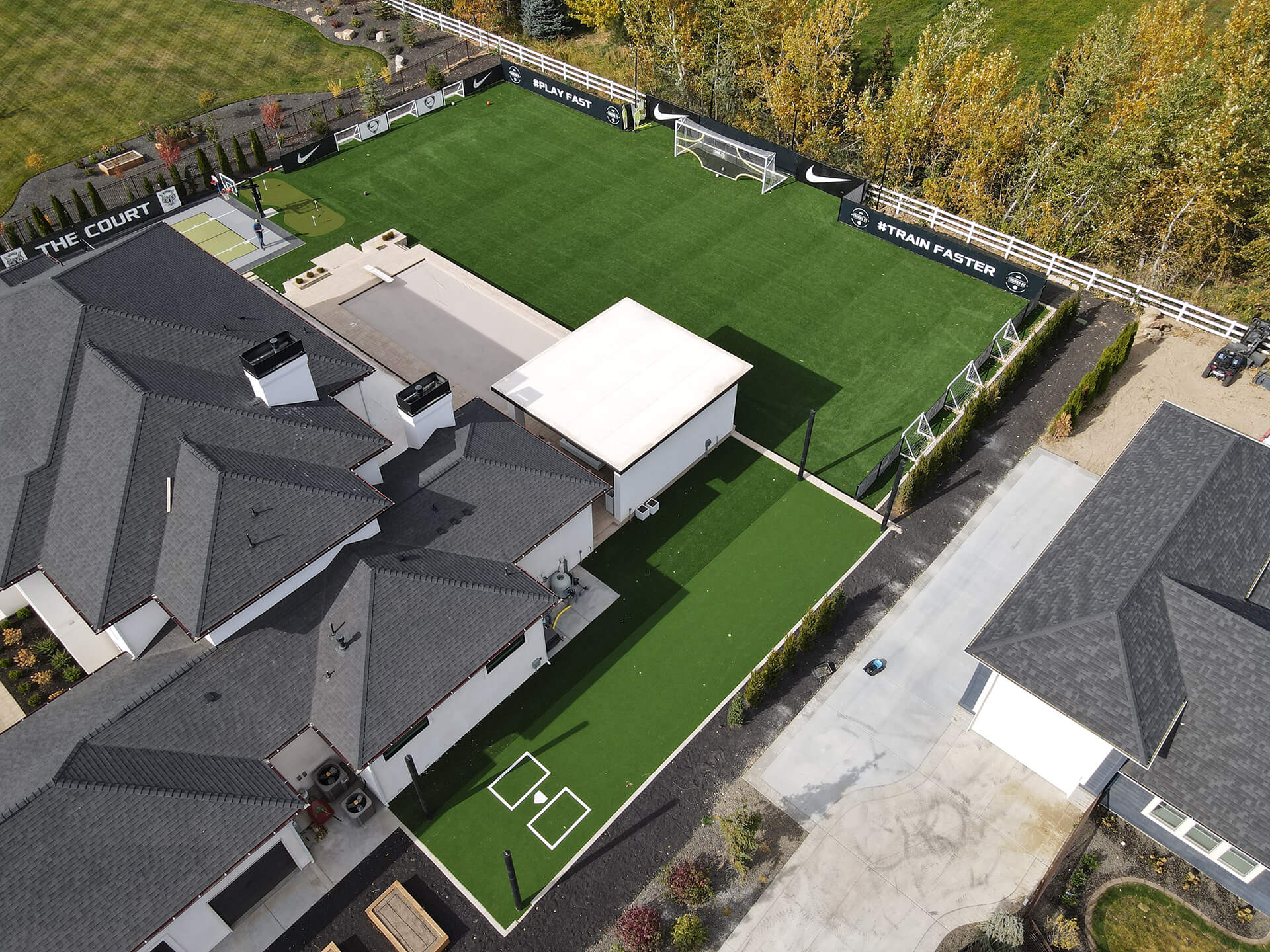 Aerial view of a large home with artificial grass lawn and basketball court